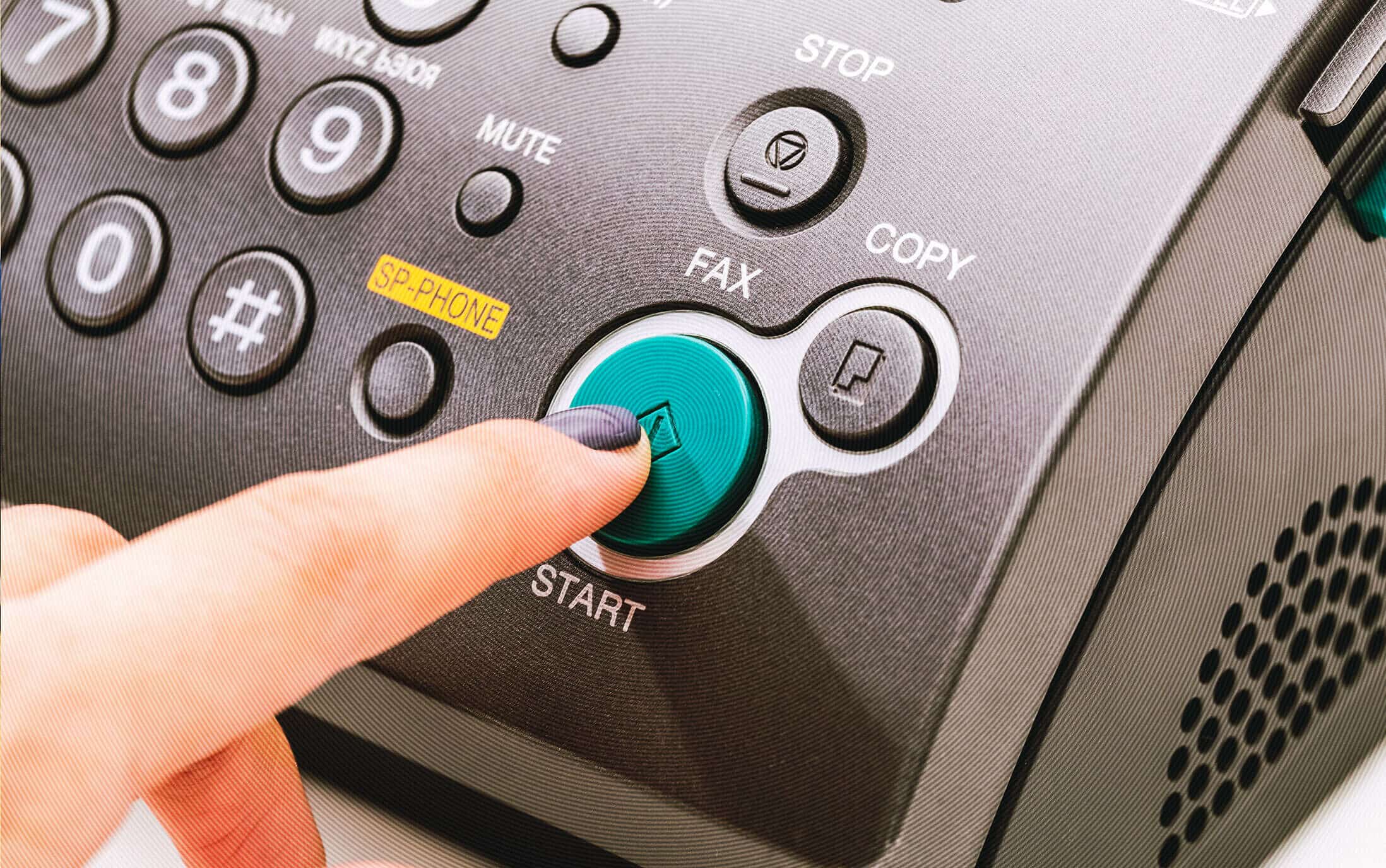 Zeigefinger tippt auf die Senden-Taste an einem Faxgerät