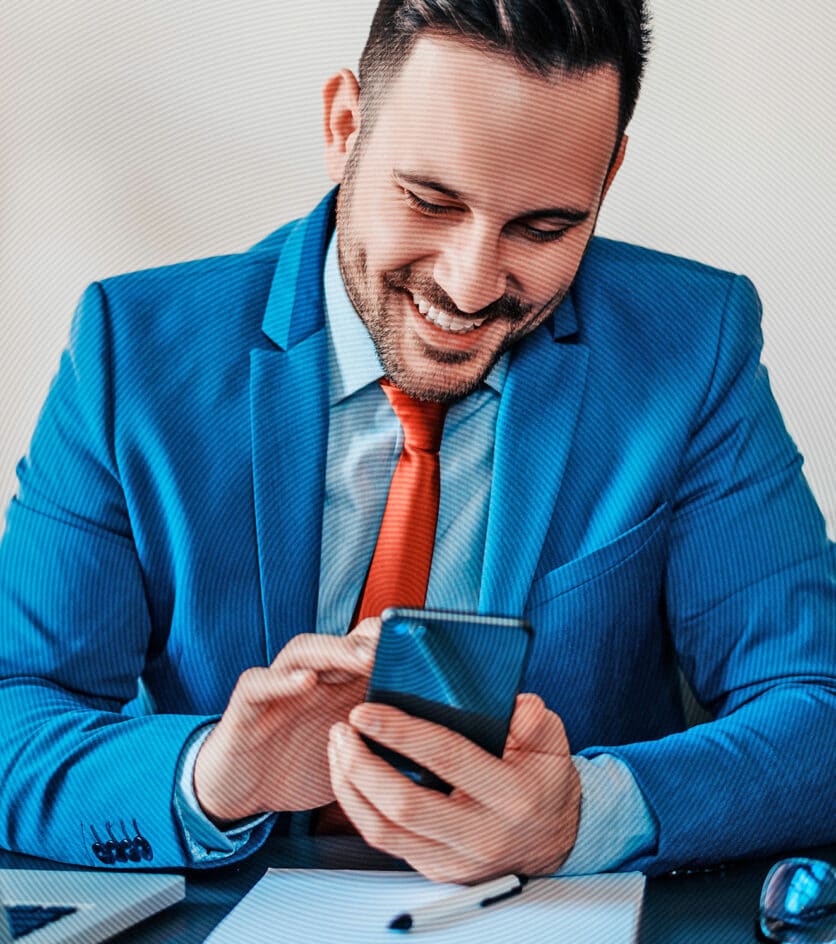 Junger Geschäftsmann im hellblauen Anzug unt roter Krawatte tippt lächelnd auf dem Smartphone