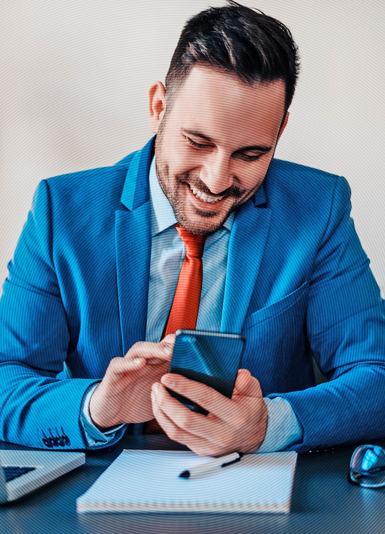 Junger Geschäftsmann im hellblauen Anzug und roter Krawatte tippt lächelnd auf dem Smartphone