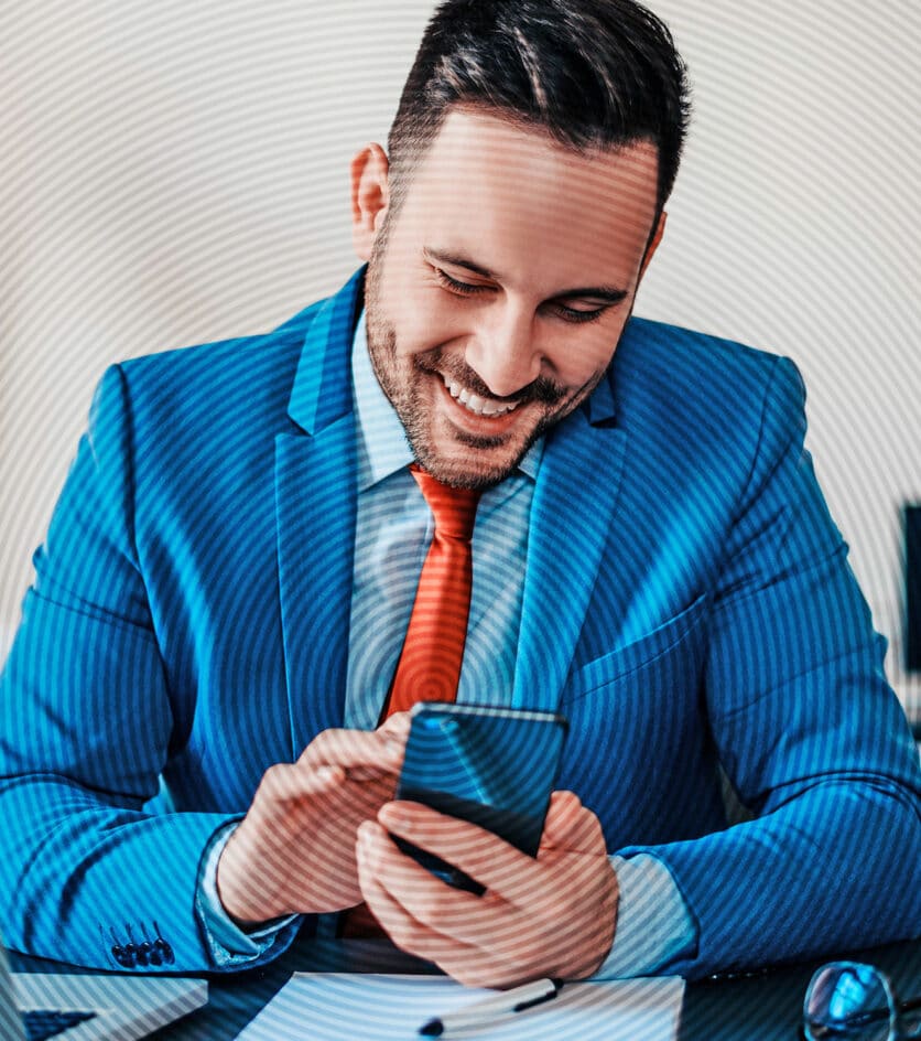 Fröhlicher Geschäftsmann im hellblauen Anzug und roter Krawatte tippt auf dem Smartphone